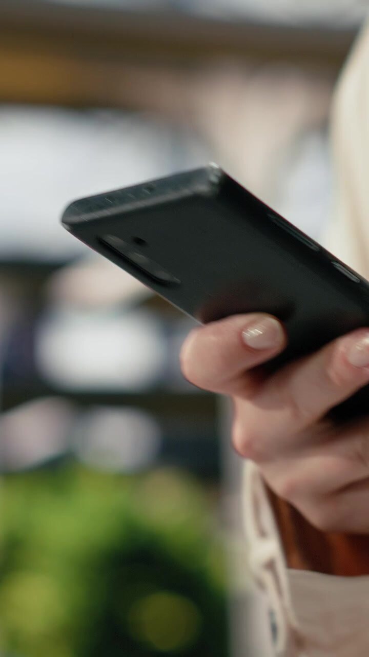 Video verticale. Primissimo piano di un viaggiatore che tiene lo smartphone mentre cammina nel terminal degli autobus.