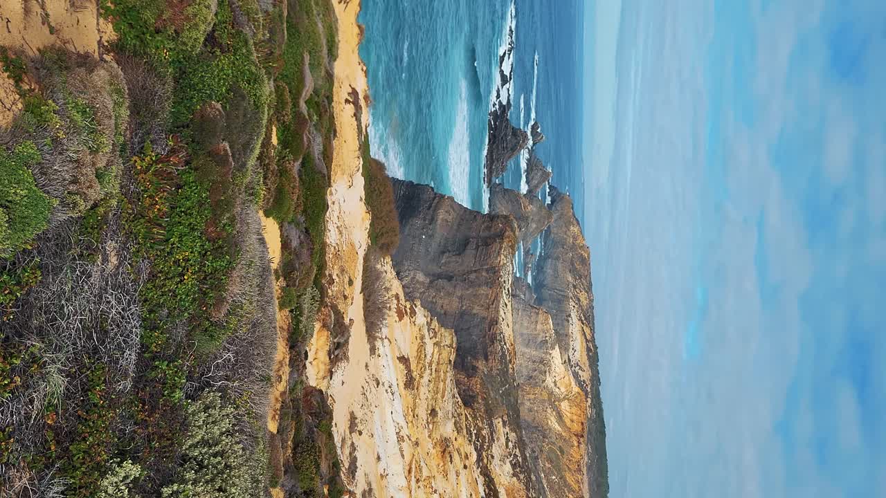 zambujeira do mar sobre la orilla del mar con olas del océano, acantilados y dunas de arena cubiertas de vegetación verde hojas rojas de higo agrio, día soleado, cielo azul claro