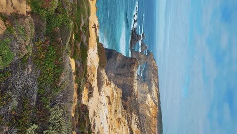 zambujeira do mar over the sea shore with ocean waves, cliffs and sand dunes covered by green vegetation red leaves of sour fig, sunny day, clear blue sky