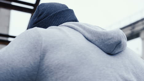 close-up view of caucasian man in grey hoodie hitting a punching bag outdoors an abandoned factory on a cloudy morning