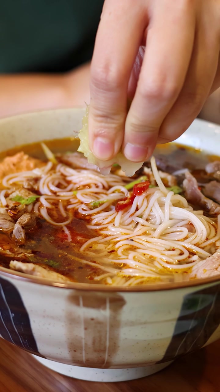 Primo piano di mani che spremono lime su una ciotola di ceramica di zuppa di noodle vietnamita tradizionale