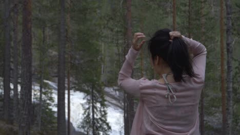 Niña-Jugando-Con-Su-Cabello-En-Un-Bosque,-Cerca-De-Una-Cascada