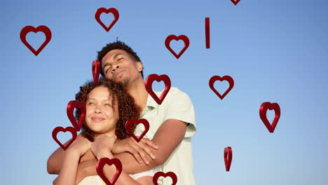 animation of hearts moving over diverse couple in love embracing on beach in summer