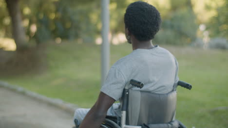 Back-View-Of-Young-Black-Man-Riding-His-Wheelchair-In-Park-On-Summer-Day