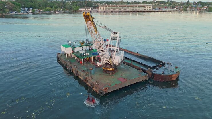Floating construction site island, crane pulls dirt out of water, aerial orbit