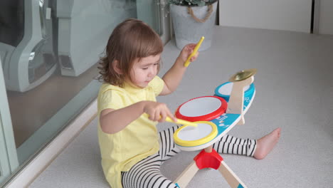 3-year-old korean-ukrainian girl sitting on floor, making music on toy drum set