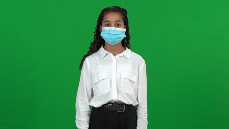 happy african american teenage girl taking off coronavirus face mask looking at camera smiling. portrait of positive teen at chromakey green screen background. the end of covid-19 pandemic concept.