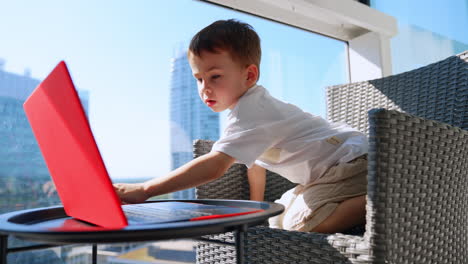 young boy engaged with a laptop indoors. a young boy is engrossed in a bright red laptop while sitting in a modern chair during the day