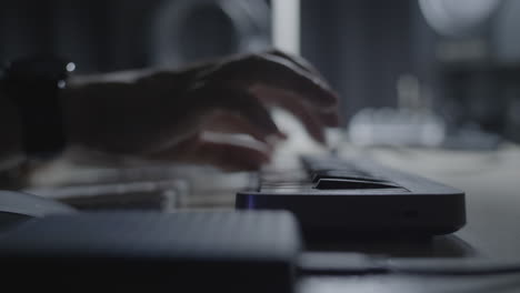 close up on producer - musician hand playing a melody riff on a midi keyboard in the studio with a dimmed light
