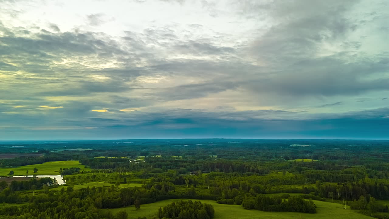 An epic aerial timelapse captures clouds moving across the sky at sunset, revealing a vast and beautiful landscape of green forests, meadows, and lakes in Latvia
