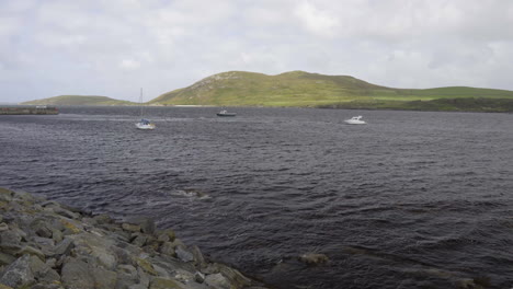 toma estática de la costa de irlanda mirando 3 barcos en un día ventoso en el océano atlántico y una isla en el fondo en 4k