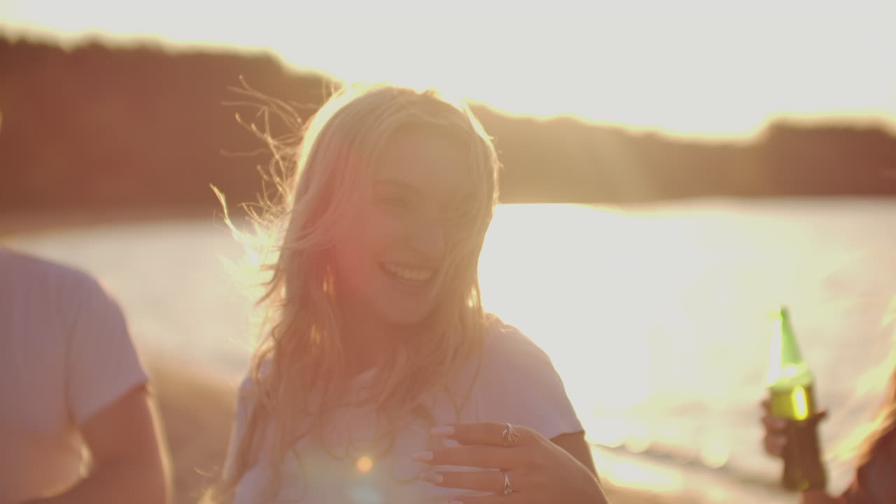A beautiful blonde girl with long hair enjoys dancing and her time on the theamy open air party with beer and the best young friends.