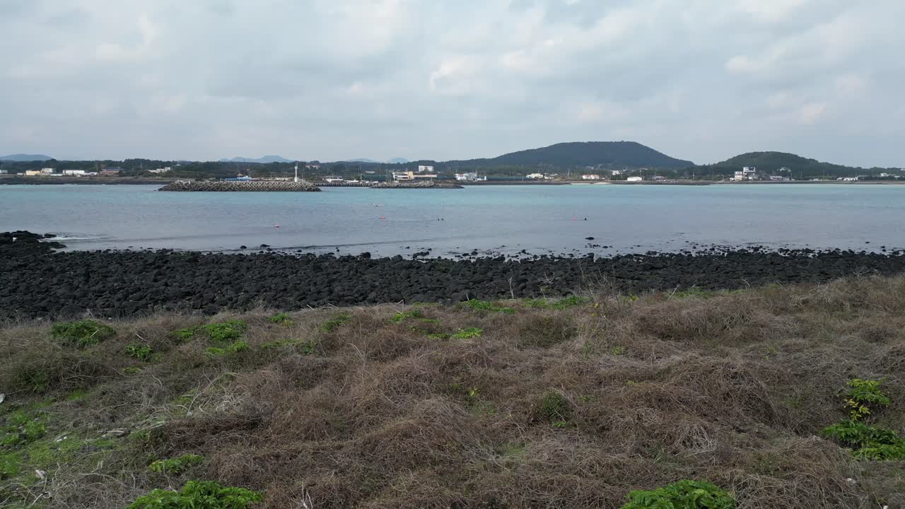 Drone aerial view in South Korea countryside flying into the sea with green island rocky area haenyeo women divers fishing jeju island cloudy