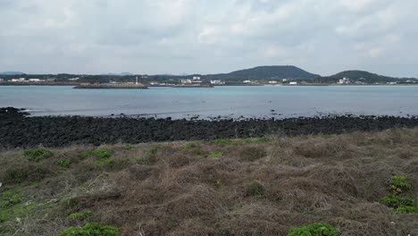 drone aerial view in south korea countryside flying into the sea with green island rocky area haenyeo women divers fishing jeju island cloudy