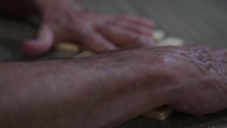 las manos del anciano fuerte mezclan dominós en un juego nocturno.