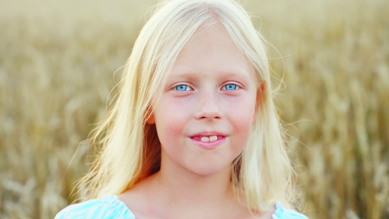 Nahaufnahme-Porträt eines glücklichen blonden Mädchens mit blauen Augen in einem Weizenfeld.