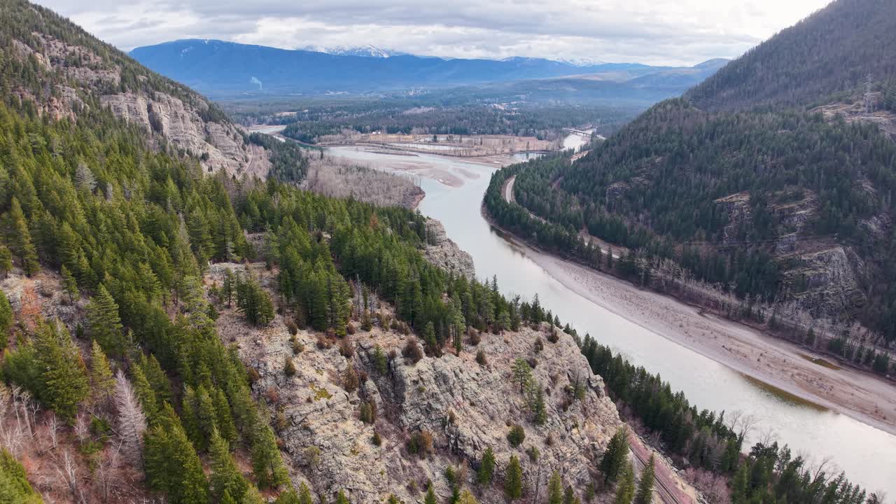 Vista drone di un fiume serpeggiante che scorre attraverso una valle tra pendii boscosi e pendii rocciosi vicino a Whitefish, Montana, con montagne in lontananza
