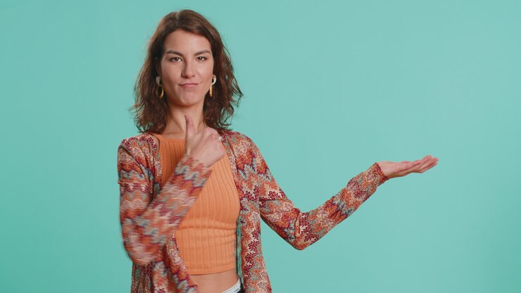 Young woman showing thumbs up and pointing at left on blank space place for your advertisement logo