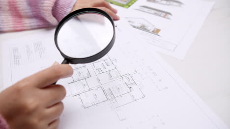 engineer using magnifying glass to examine architectural blueprints