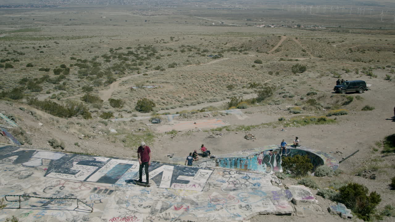 Skateboarding and graffiti at an abandoned desert structure with a view of wind turbines