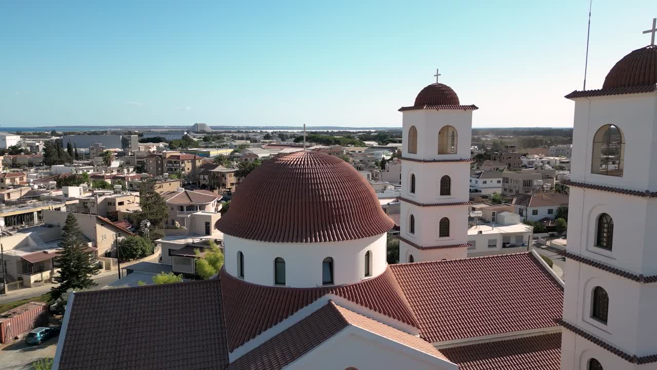 Vista aerea di una chiesa con cupola e campanile a Limassol, Cipro. Case vicine e la costa sono visibili sotto un cielo luminoso. La scena cattura il paesaggio urbano della zona.