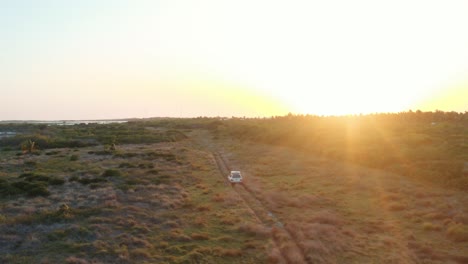 Sehr-Breite-Luftaufnahme-Eines-Geländewagens-Mit-Einem-Dachzelt,-Das-Durch-Ein-Raues-Feld-In-Richtung-Sonnenuntergang-Fährt