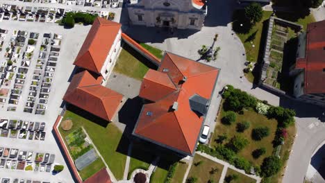 Toma-Aérea-De-Arriba-Hacia-Abajo-De-La-Catedral-Con-Cementerios-En-El-Cementerio-De-Menges,-Eslovenia-Durante-El-Verano