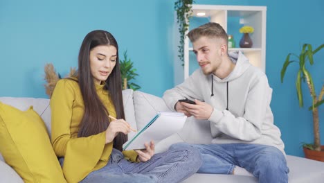 Young-man-and-young-woman-sitting-on-sofa-at-home-making-a-list.