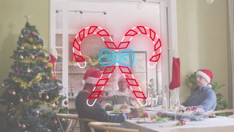 Animation-of-candy-cane-icon-over-diverse-friends-sitting-at-table-at-christmas