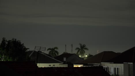 night view of houses, palm trees, antennas, and towers under a dark sky