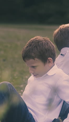 classmates wearing shirts and jeans lean backs sitting on large green lawn on warm day close view slow motion