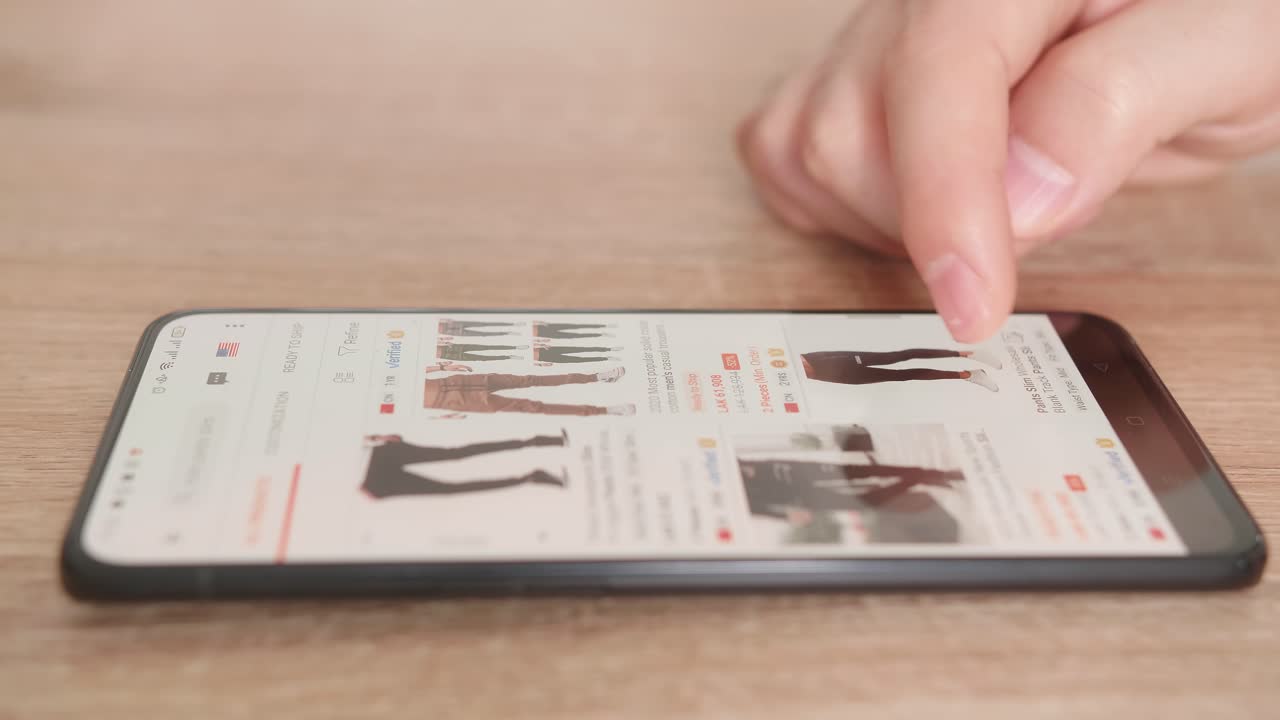 Man Looks At The Goods In The Online Clothing Store. People Using Smartphone, Online Shopping. Male Is Choosing Pants