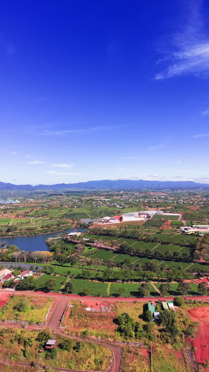 The wide view of Lam Dong, Vietnam, with green farms and fields. The sky is clear, and the scene captures the land's natural beauty with hills and water