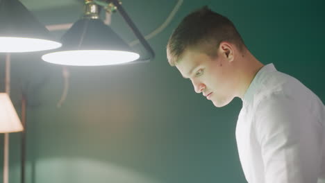 close-up side shot of gentleman in white shirt walking into billiard room with modern interior, overhead lamps, and green walls. focused expression, sleek atmosphere, ambiance of the gaming area