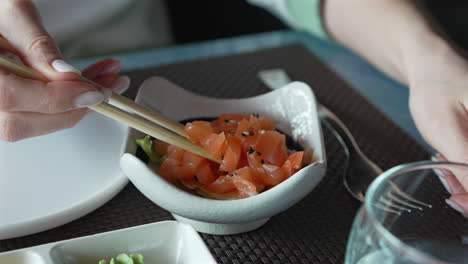 una mujer con palillos en la mano toma un pedazo de tartare de salmón con sésamo y hierbas