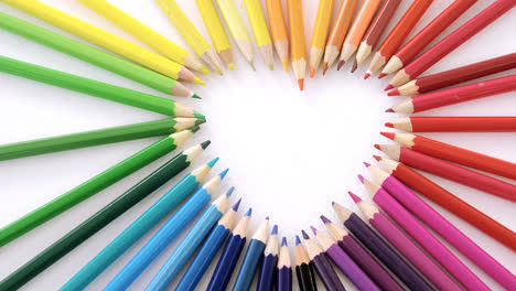 colored pencils arranged in heart shape on white background