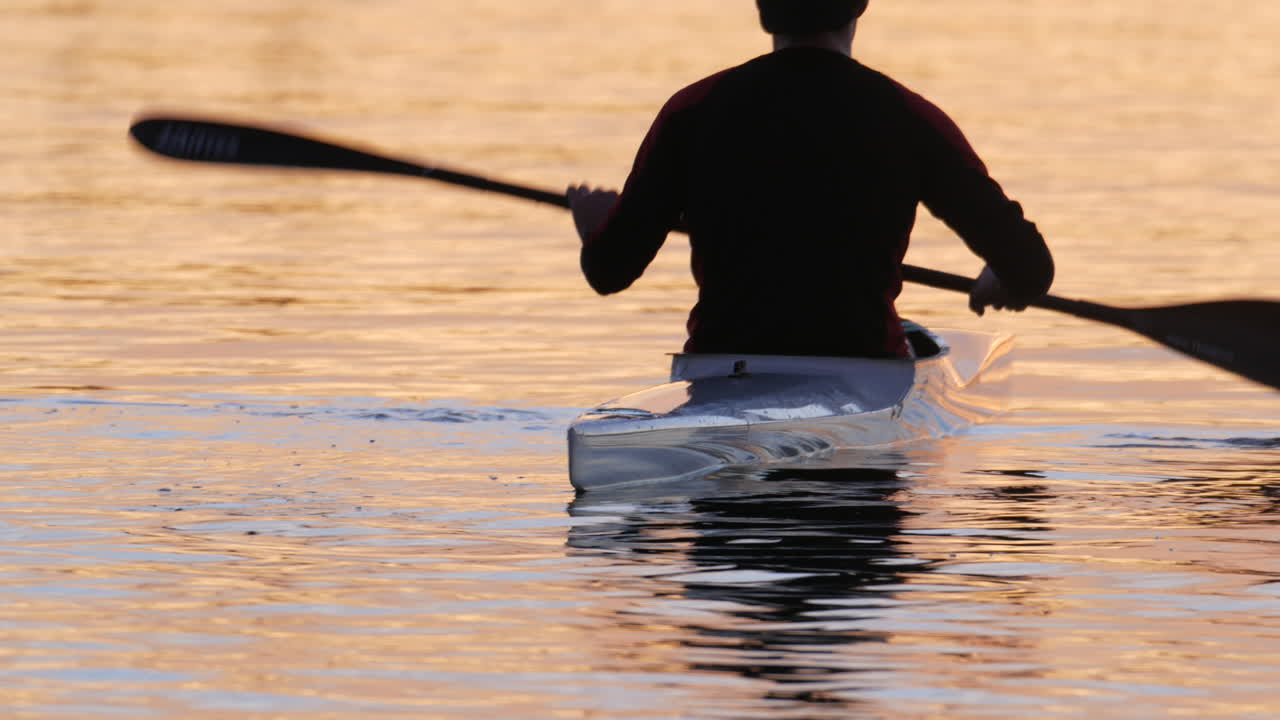 un hombre balanceándose en su kayak de carreras descansando entre intervalos durante una sesión de entrenamiento con un hermoso amanecer reflejándose en el agua en varsity lake gold coast qld australia