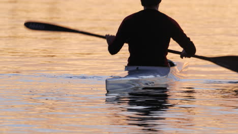 A-Man-balancing-in-his-racing-kayak-resting-in-between-intervals-during-a-training-session-with-a-beautiful-sunrise-reflecting-off-the-water-at-Varsity-Lake-Gold-Coast-QLD-Australia