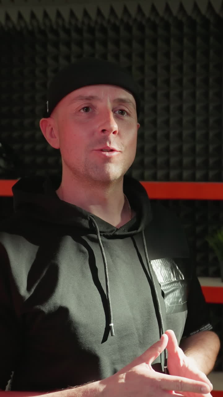 검은 옷을 입은 남자가 은색과 검은색의 스튜디오 배경에 표시적인 손짓으로 활기찬 대화를 나누고 있습니다.