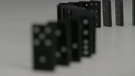 row of black dominoes with white spots falling in studio