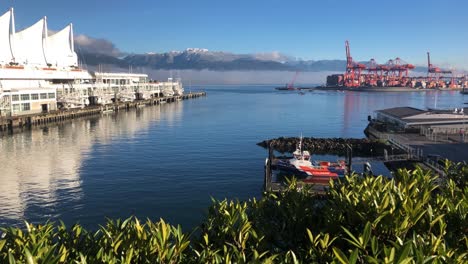 seabus departing from the harbour of vancouver with in the background a container terminal with gantry cranes working on a containership on a sunny day