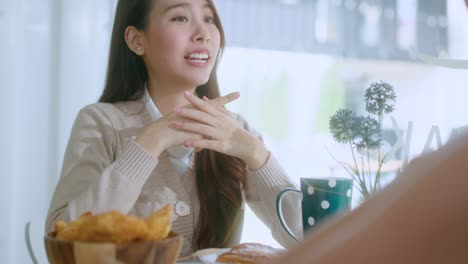 매력적인 아시아 여성은 미소 짓고 웃으며 친구들과 좋은 긍정적 인 대화를 나누고 카페의 창문 근처의 카운터에서 정원에서 낮빛으로 긍정적인 태도 관계를 유지합니다.