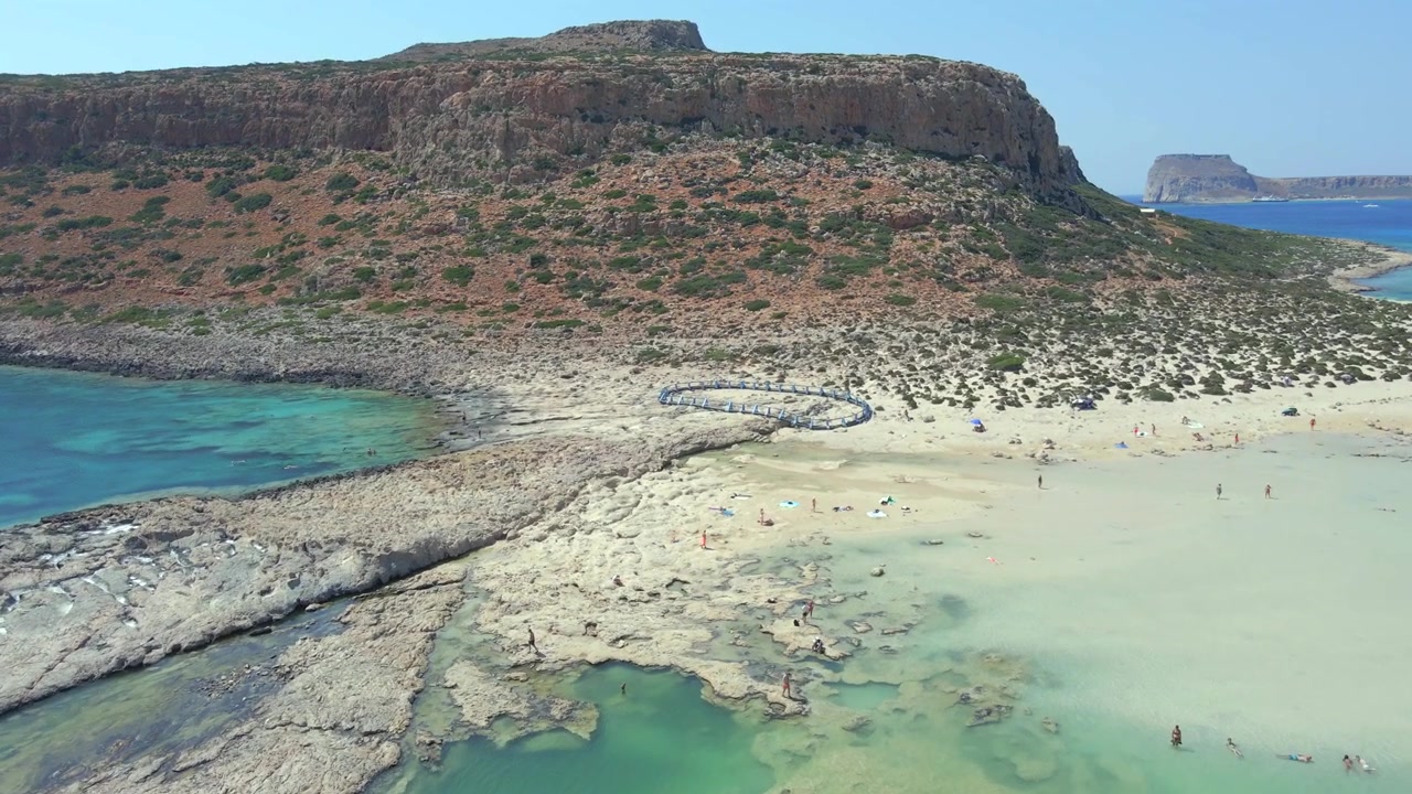 Naturskønt dronebillede i lav højde, der bevæger sig fremad over naturlige klippebassiner og turkist vand mod den massive klippe ved Balos-lagunen på Kreta, Grækenland. Smukt eksotisk paradislandskab, dagtid.