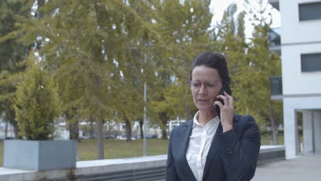 dolly shot of a happy businesswoman in office suit talking on cellphone and making winner gesture while walking outside