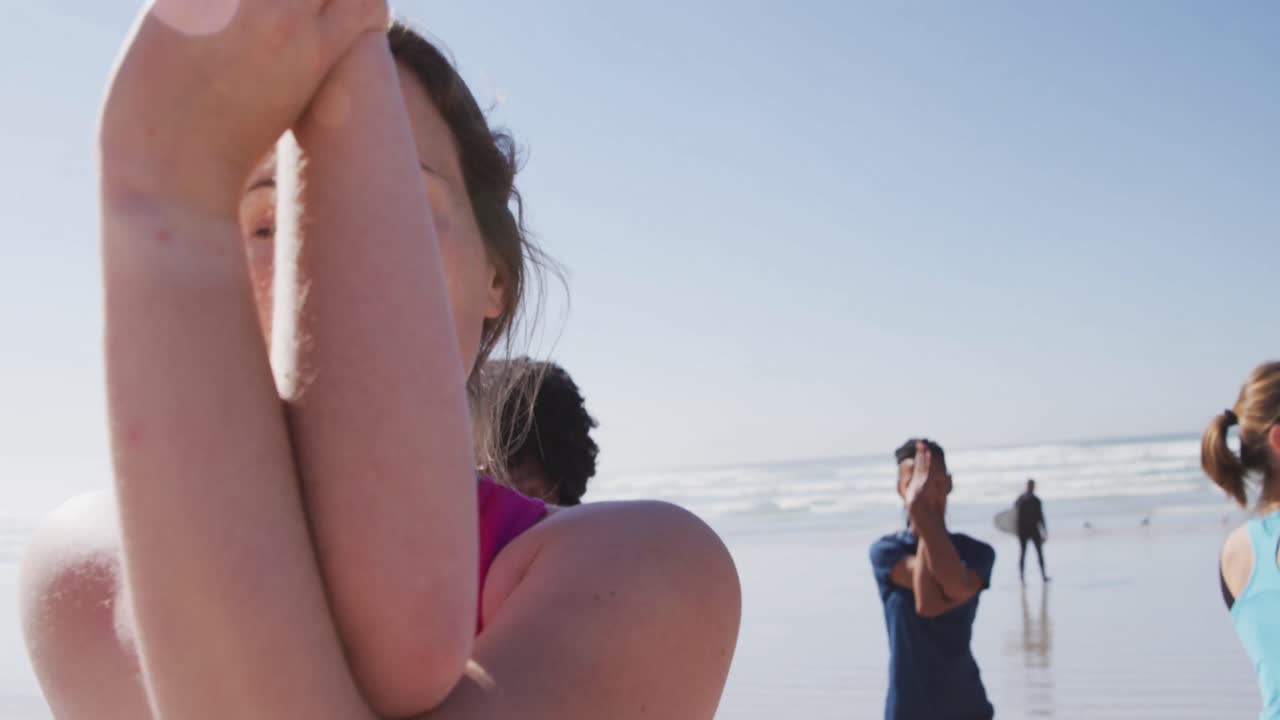 mujer caucásica haciendo yoga en la playa con un grupo de mujeres y fondo de cielo azul