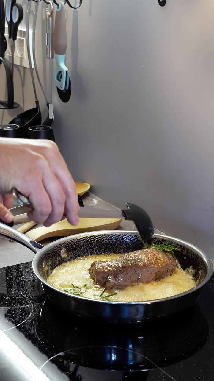 Pan-frying juicy rib-eye steak by basting it with sizzling hot butter. Vertical