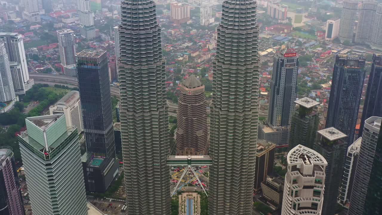Aerial tilt down shot of Kuala Lumpur Twin Towers showcasing the marvellous structure engineering inspired by Malaysian Muslim Heritage, revealing the Suria Shopping mall and the luscious KLCC park