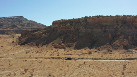 Aerial-following-fast-moving-car-down-dirt-road-in-desert-with-rock-formations