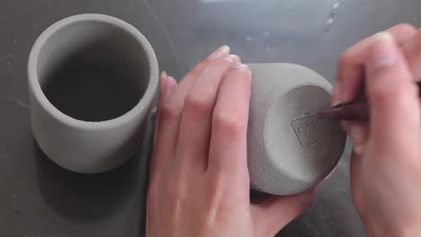punto de vista de la artista alfarera tallando la firma en la superficie inferior de una taza