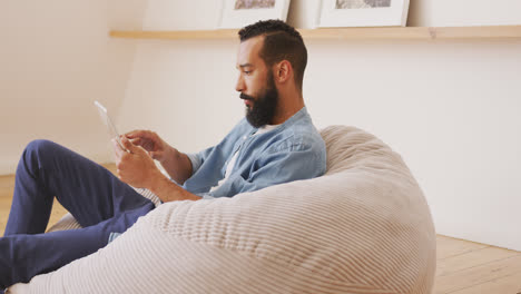 Nachdenklicher-Mann-Mit-Digitalem-Tablet-Beim-Entspannen-Auf-Einem-Sitzsack-Im-Innenbereich